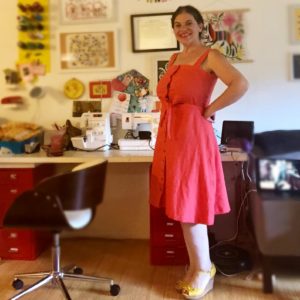 A woman smiles at the camera while wearing a coral-colored sundress.