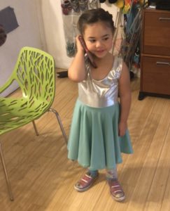A little girl in a blue-skirted dress with a silver bodice, holding a phone to her ear