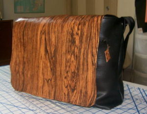 Black vinyl messenger bag with a woodgrain-patterned vinyl flap.