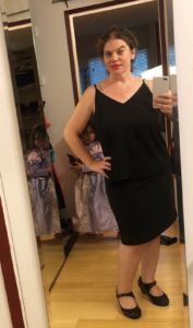 A woman wears a black tank top and gray skirt.