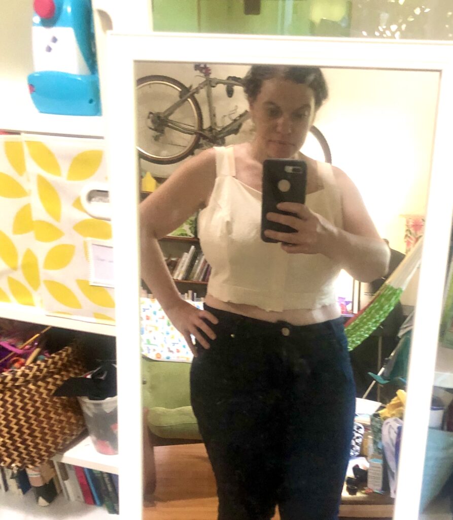 A white woman wears a semi-completed bodice made of cream-colored muslin.