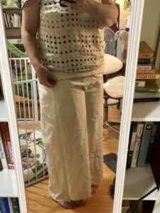 A woman wears a pair of cream-colored pants in front of a mirror. They fit poorly around the pelvis.