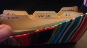 The striped pouch contains tiny index card-sized files, labeled "Hotel," "Flight," "Ground," and "Air"